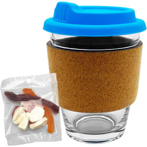 A glass coffee cup with a cork band and a blue lid, accompanied by a packet of mixed lollies in various colours.