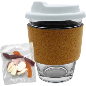 A glass coffee cup with a cork band and a white lid, alongside a bag of mixed lollies in various colours.