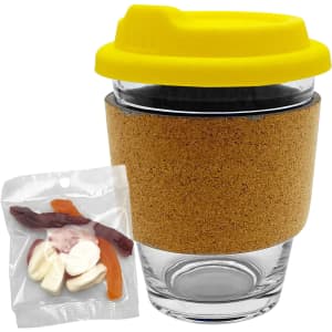 A glass coffee cup with a cork band and yellow lid, accompanied by a bag of mixed lollies in various colours.