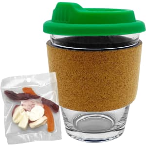 A clear glass coffee cup with a green lid and cork band, accompanied by a pack of mixed lollies in assorted colours.