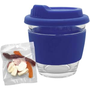 A clear glass coffee cup with a blue silicone lid and grip, accompanied by a bag of mixed lollies.