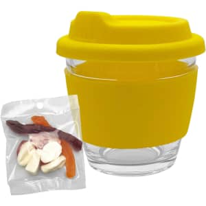 A clear glass coffee cup with a yellow silicone lid and sleeve, accompanied by a bag of mixed lollies.