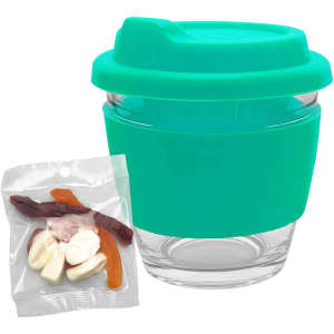 A clear glass coffee cup with a teal silicone lid and sleeve, accompanied by a packet of mixed lollies.