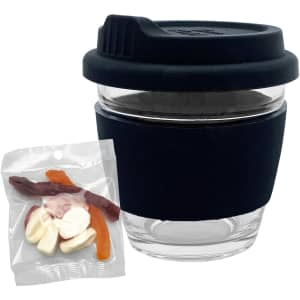 A clear glass coffee cup with a black lid and sleeve, beside a packet of mixed jelly lollies in various colours.