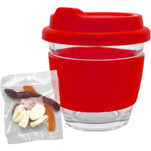 A transparent glass coffee cup with a red silicone lid and sleeve, alongside a pack of mixed jelly lollies.