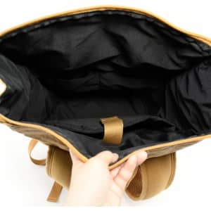 A laptop backpack with a kraft paper exterior and a spacious black interior, featuring compartments and a branding logo.
