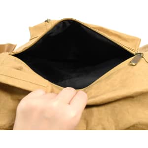 A hand reaching into a tan kraft paper laptop backpack, revealing a black interior and a zippered opening.
