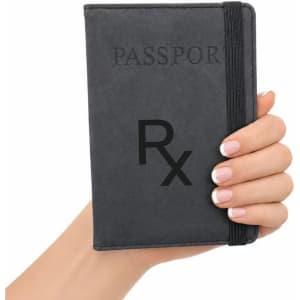 A grey passport wallet is held in a hand, featuring a band for secure closure and a logo on the cover.