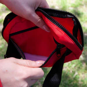 A red bum bag with a zippered opening, showcasing its inner pocket and fabric details. Contains a logo.