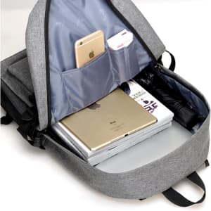 A grey laptop backpack with an open compartment displaying a laptop, magazines, and a mobile phone in pockets.