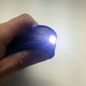 A blue 360 Degree Torch held in a hand, emitting a bright light from its front end.
