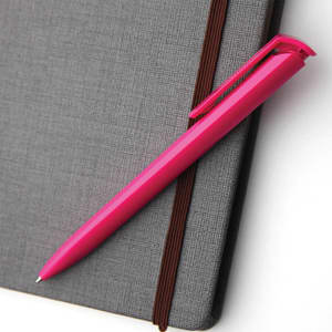 A pink plastic pen rests on a grey textured notebook, featuring a clip and smooth barrel design.