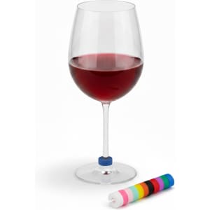 A red wine glass with a blue wine glass marker beside a roll of colourful markers. The glass is elegantly shaped.