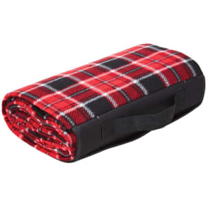 A rolled red and black plaid picnic rug with a carrying handle. The rug features a soft fleece material.