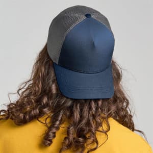 A trucker cap in navy with a mesh back, featuring a logo, worn by a person with curly hair.