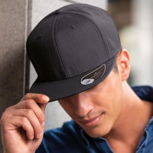 A black cap with a flat peak, featuring a logo, worn by a man with a slight smile.