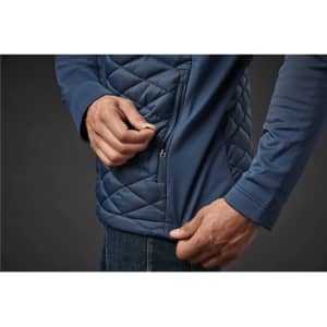 A close-up of a person adjusting the zip on a navy thermal shell jacket with a quilted design.