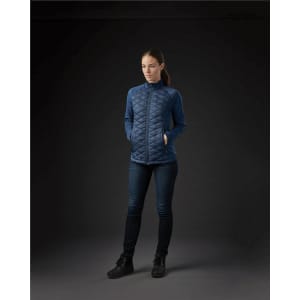 A women's boulder thermal shell jacket in dark blue with a quilted design and pockets, displayed against a dark background.