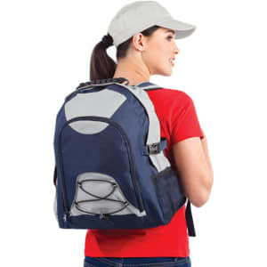 A person wearing a grey and navy Climber Backpack, with a red shirt and cap, posing from the side.