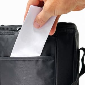 A drink bottle cooler in black with a hand placing a letter into its front pocket. It features a zipper and side handle.