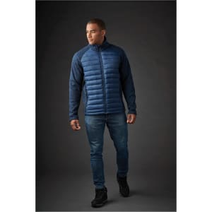 A men's hybrid jacket in navy blue, featuring a padded front and textured sleeves. The model is wearing jeans and black shoes.