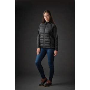 A woman wearing a black and grey Women's Narvik Hybrid Jacket with a fitted design, paired with jeans and boots.