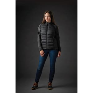 A woman wearing a black hybrid jacket with a padded front and textured sleeves, paired with denim jeans.