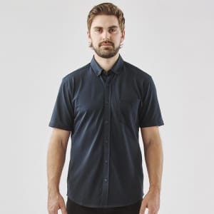 A man wearing a navy blue short sleeve button-up shirt with a pocket and a logo on the chest.