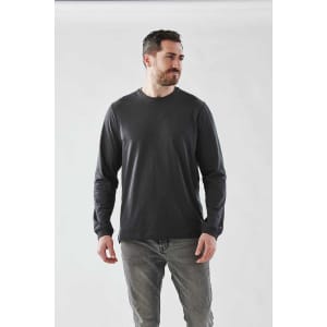 A man wearing a long sleeve tee in dark grey, paired with light grey jeans, against a plain background.