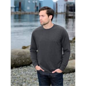 A man wearing a charcoal long-sleeve t-shirt, standing by a waterfront with colourful buildings in the background.