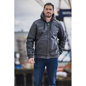 A man stands wearing a grey hooded jumper. The hoodie features a logo and has a zipper and drawstring.
