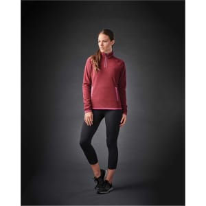 A woman wearing a burgundy women's fleece jumper with a 1/4 zip and black leggings, featuring a branding logo.