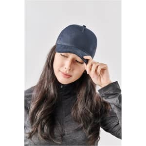 A navy trucker cap with a curved brim, featuring a logo on the front, worn by a woman with long hair.