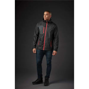 A man wearing a black rain jacket with red accents, standing against a dark background. The jacket has a logo.