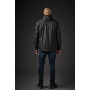 A man wearing a black rain jacket, viewed from the back, paired with dark jeans and shoes. The jacket has a hood and logo.