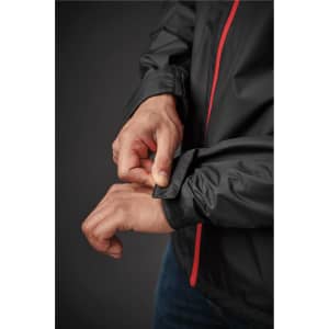 A close-up of a person adjusting the cuff of a black rain jacket with red accents. The jacket features a logo.