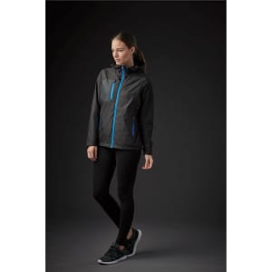 A woman wearing a black rain jacket with blue zippers, paired with black leggings and sporty shoes, against a dark background.
