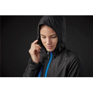 A woman wears a black rain jacket with a hood, featuring blue accents and a logo.