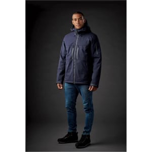 A navy jacket with a hood and zippers, worn by a model against a dark background. The jacket features a logo.
