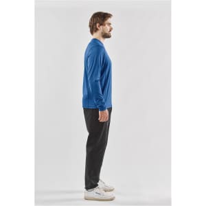 A man models a long-sleeve crew neck shirt in blue, paired with black pants. The shirt features a logo.