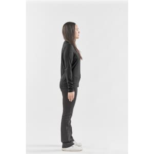 A side view of a woman wearing a black long-sleeve crew neck shirt and black pants, standing on a plain background.