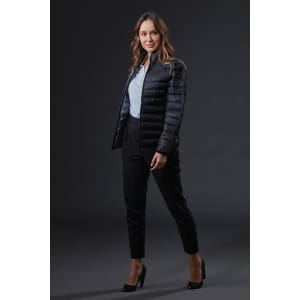 A woman in a black puffer jacket poses against a dark background, wearing tailored black trousers and high heels.
