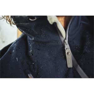 A close-up of a navy softshell jacket with visible water droplets on the fabric and a branded zipper.