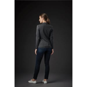 A woman wearing a dark grey knit blazer, paired with dark jeans and white shoes, facing away from the viewer.