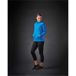 A woman wearing a bright blue lightweight softshell jacket with pockets, paired with black leggings and shoes.