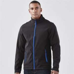A man wearing a black softshell jacket with blue accents and zippered pockets, featuring a logo.