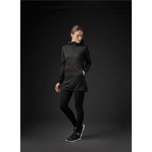A woman wearing a black softshell jacket, black leggings, and athletic shoes, standing against a dark background.