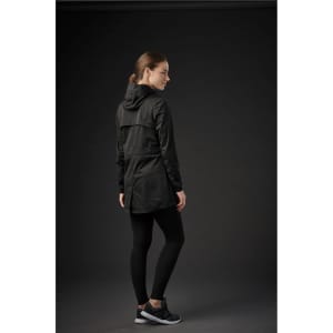 A woman in a black softshell jacket with a hood, paired with black leggings and trainers, facing away from the camera.