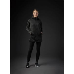 A woman wearing a black Women's Belcarra Softshell jacket, paired with black leggings and sneakers. The jacket features a hood and pockets.