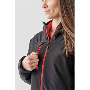 A woman models a black and red insulated softshell jacket with a zipper and hood. The jacket has a subtle logo.